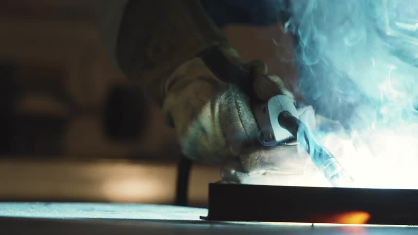 Hand with glove welding a metal object and sparks coming out