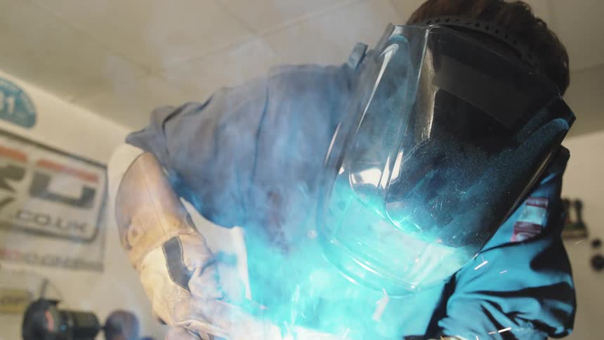 A person in a welding mask and protective suit welds