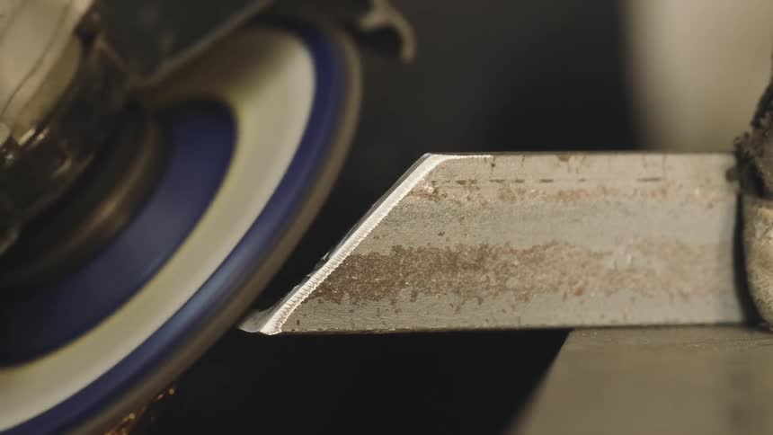 A rotating disk tool scraping the edge of a metal object and releasing several bright sparks