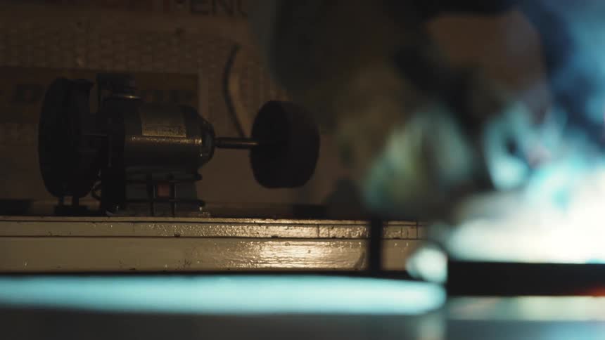 Grinding machine appears blurred in the background while welding takes place in the foreground with intense blue light