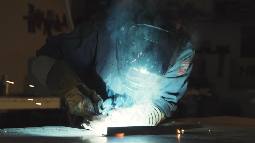 A man welding an iron bar on top of a workbench