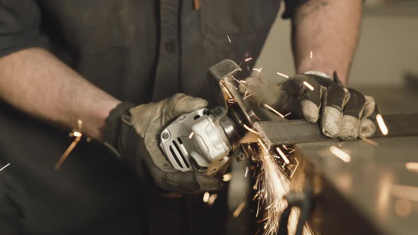 Pair of gloved hands handling a cutting tool on a metal sheet