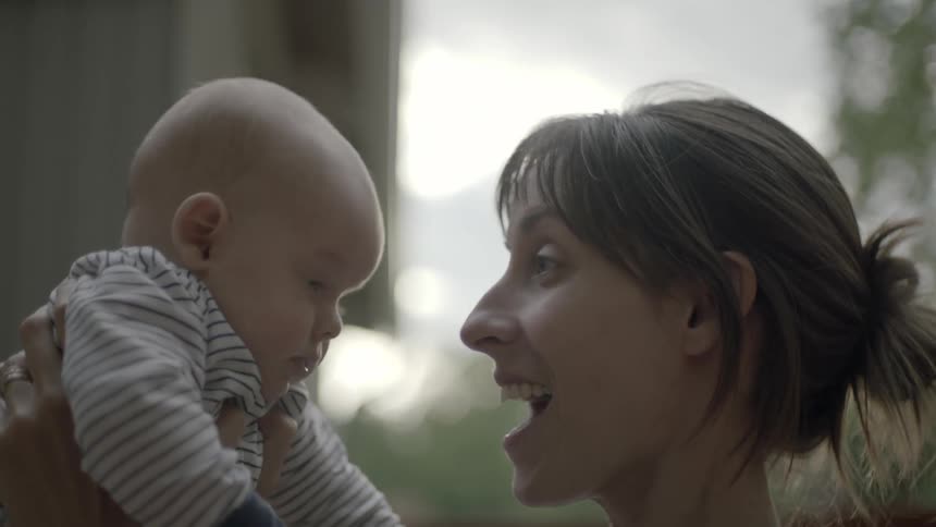 A woman is holding a baby up high and speaking to it