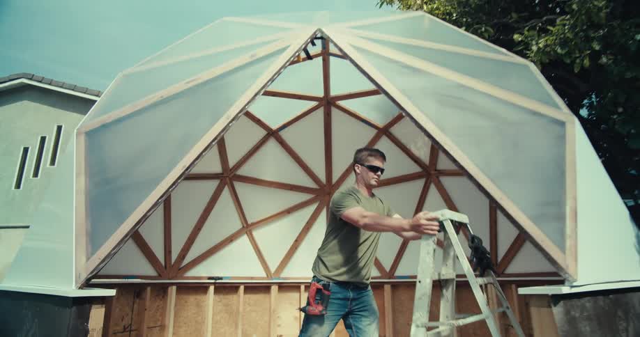 Man on ladder assembling a geometric dome in a suburban backyard