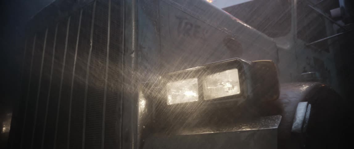 A closeup shot shows the front and side of a darkcolored truck being sprayed with water with the headlights on