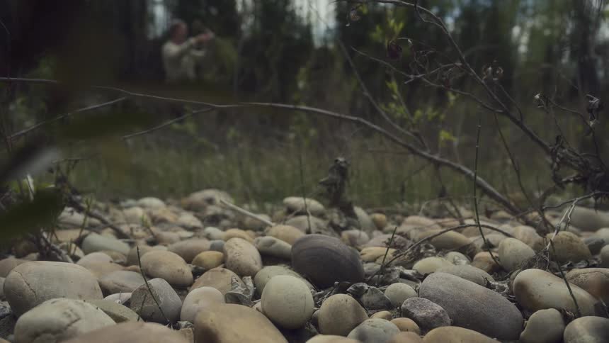 Close up fo smooth rocks in the wilderness as a man cuts twigs in the background