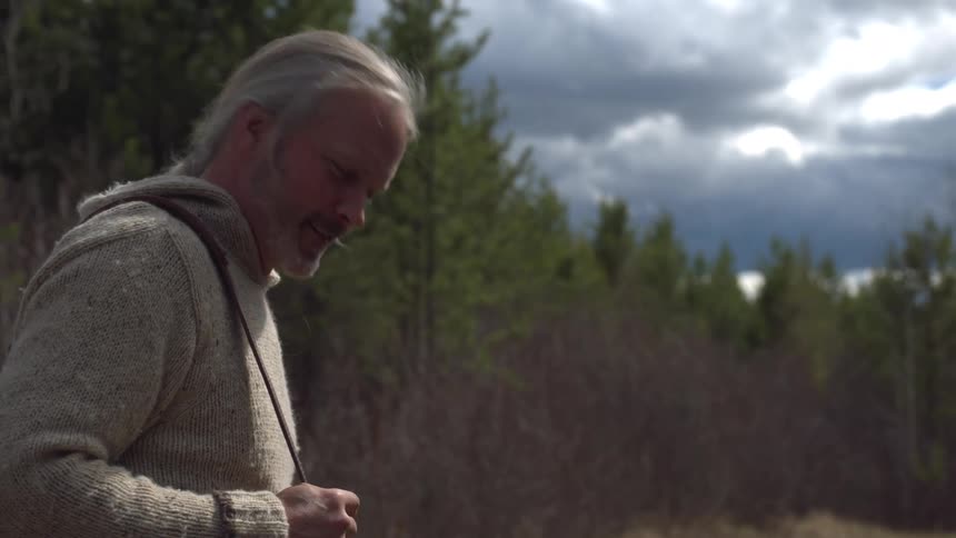 A man holding a rifle walks along a forest path at midday