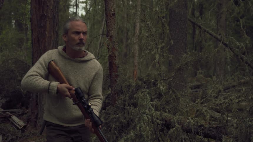 Hunter carrying a rifle preying through the forest