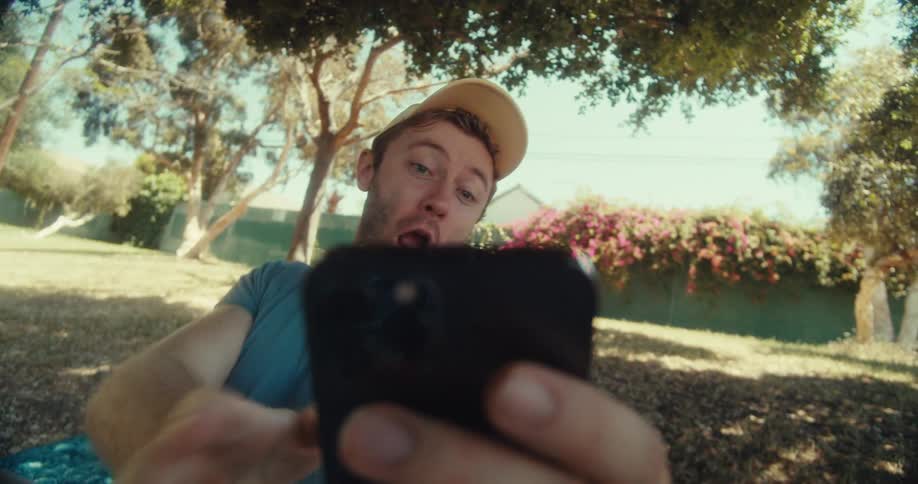A man holds his phone taking selfies with different gestures in a public park at midday