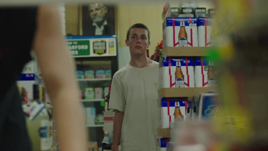 Teenager stealing food from a store and a boy in the background watching the scene