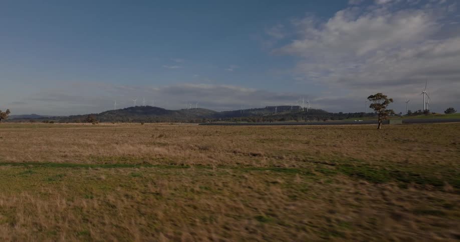 Revealing a solar farm with grass plains wind mills and some hills on the horizon