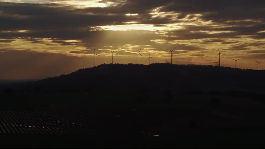 The sun is setting on the mountain full of windmills