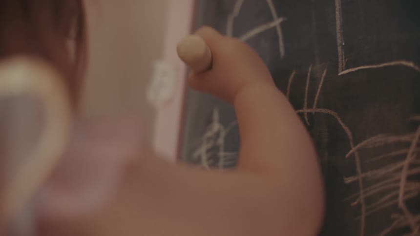 A child holds a chalk and draws on a chalkboard