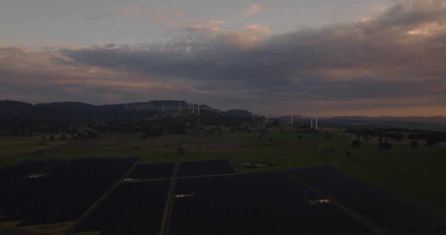 Aerial view of hills and mountains with solar panels in the forground and wind turbines in the background