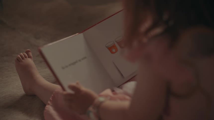 A girl is reading through a childrens book while seated on the carpet floor