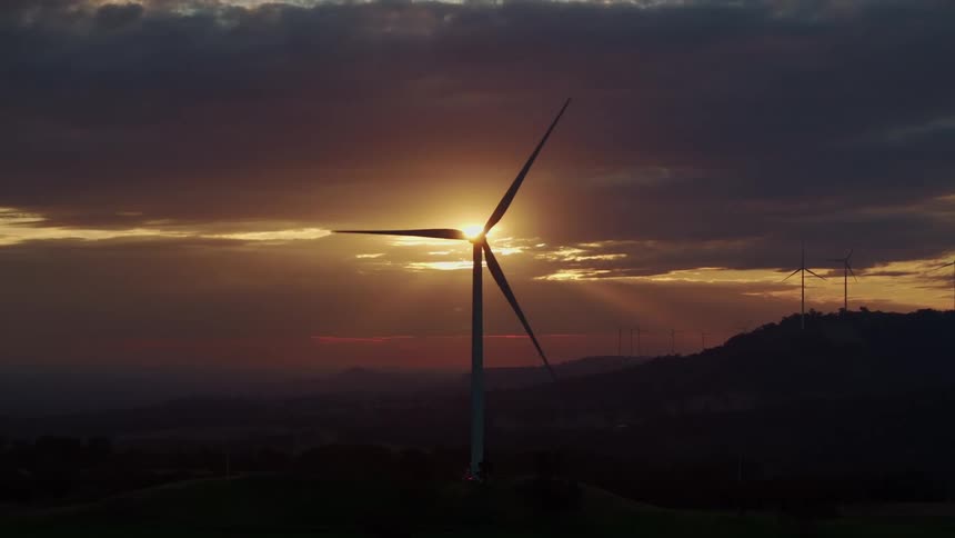 A large windmill covers the setting sun
