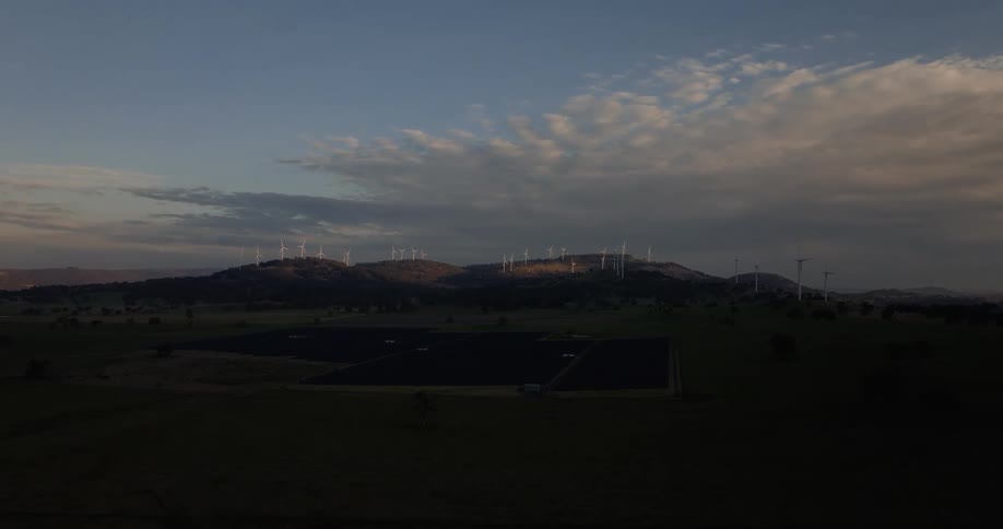 A landscape shows a combination of a solar farm and wind turbines under a twilight sky