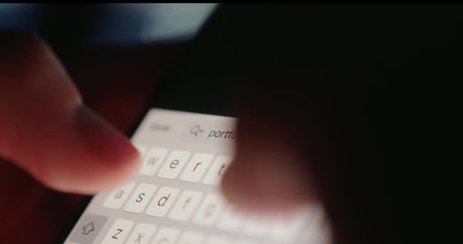 Fingers type on a brightly illuminated smartphone keyboard in a dimly lit area