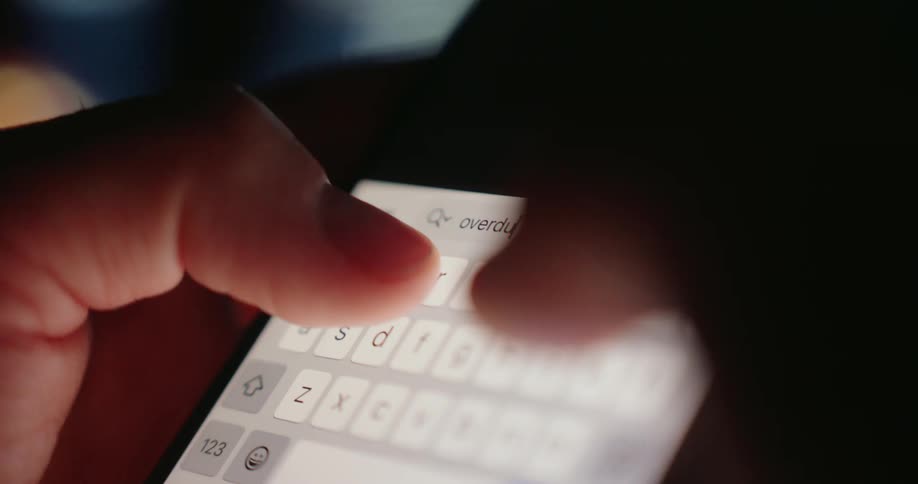 Fingers typing overdue on a smartphone in the dark