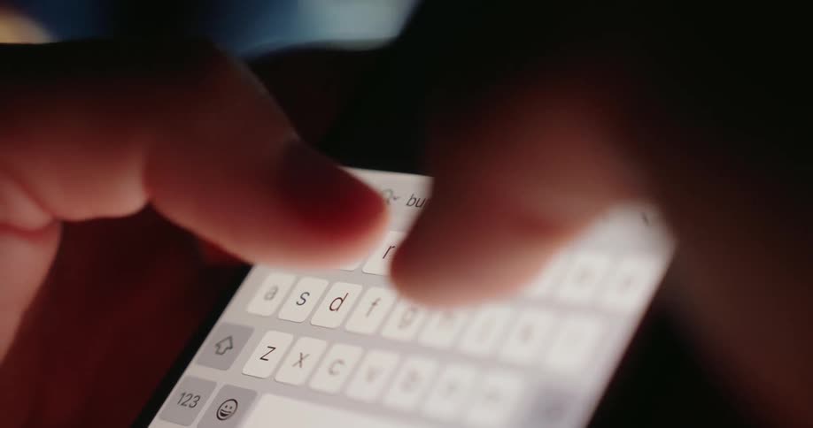 Hands of a person typing on a mobile phone in a dark room