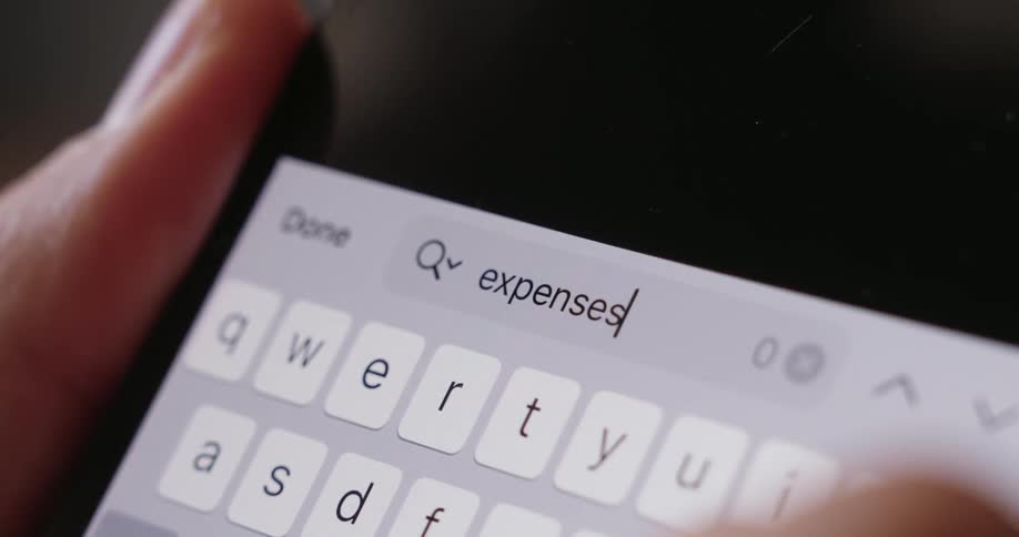 Fingers type the word expenses on a brightly illuminated smartphone keyboard