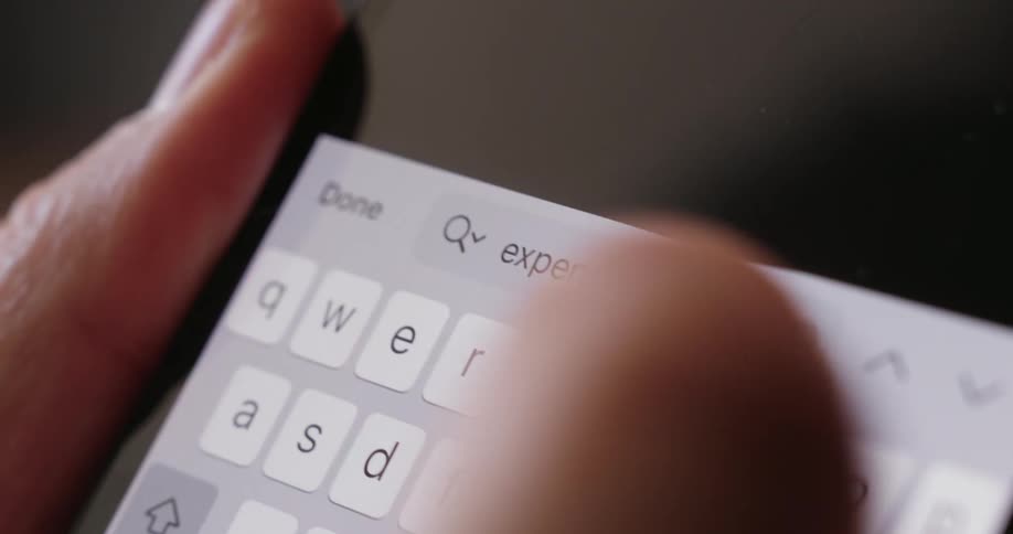 A person holds a smartphone and types the word expenses on it