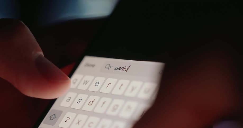 Fingers type on a brightly illuminated smartphone keyboard in a dimly lit area