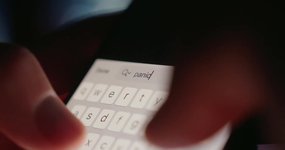 A person uses their thumbs to type panic into the phones search engine