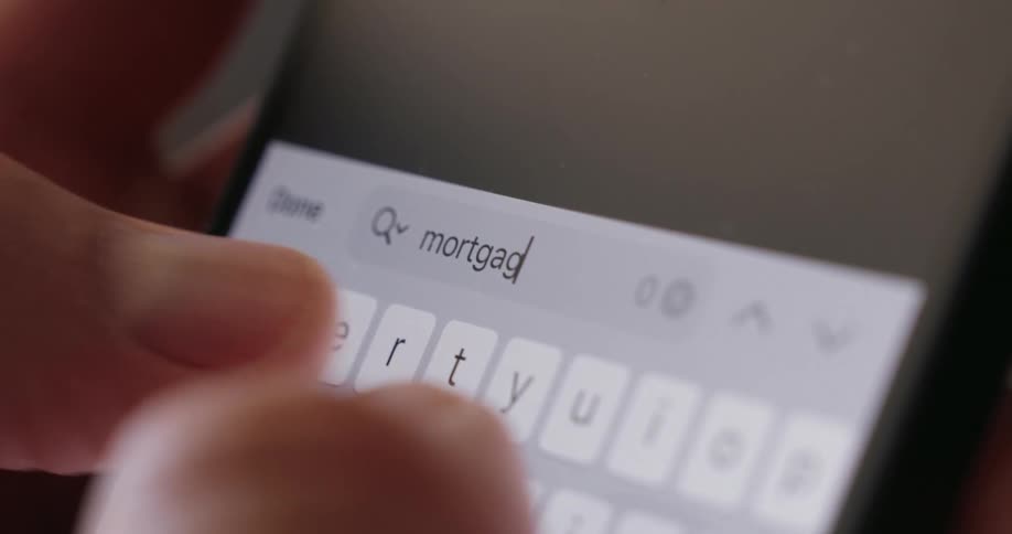 A persons arm holds a smartphone and types mortgage on the screen