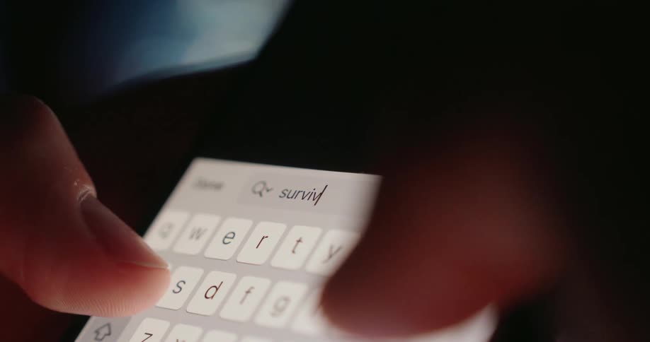 A person uses their thumbs to type the word survival into the phone search engine