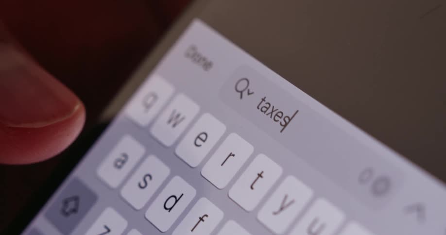 Fingers type the word taxes on a brightly illuminated smartphone keyboard