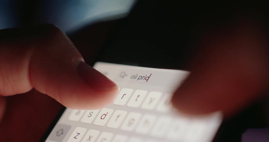 Closeup of fingers typing oil prices on a smartphone showing focused activity