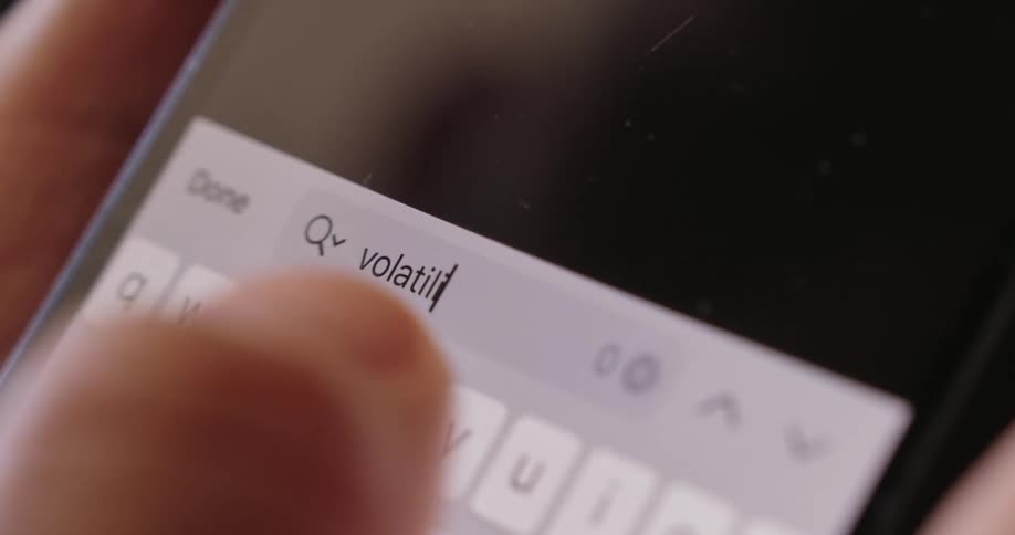 A person typing the word volatility on their phone