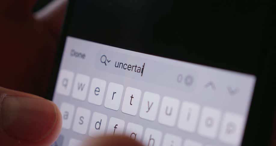 A person types the word uncertainty into the cell phone search engine