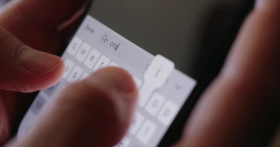 A person types the word crisis on a smartphone keyboard in a closeup shot