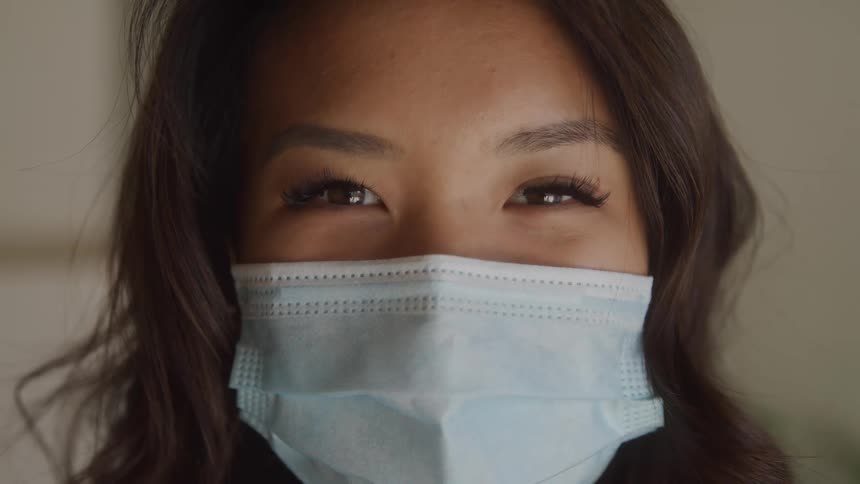 Dark haired woman faces the camera wearing a blue surgical mask