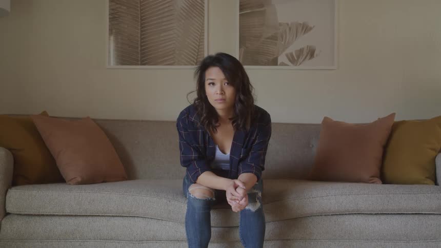 A woman sits on a sofa leaning forward with a thoughtful gaze