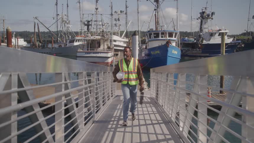 A man in safety gear is waking up a ramp away from boats in the marina