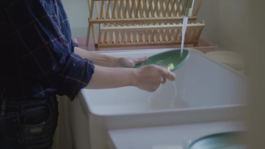A woman washes dishes at the sink but drops a plate in the sink in pain