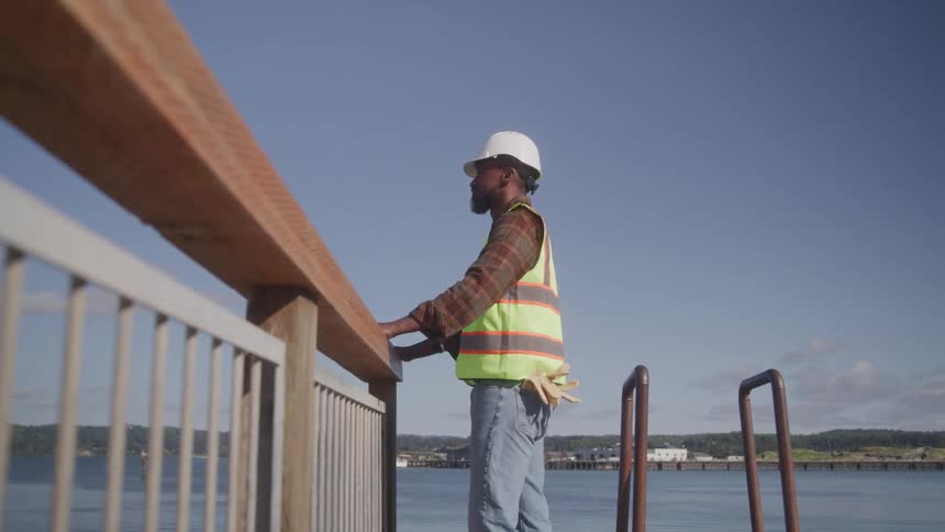 A construction worker stands on a dock looking out over the water