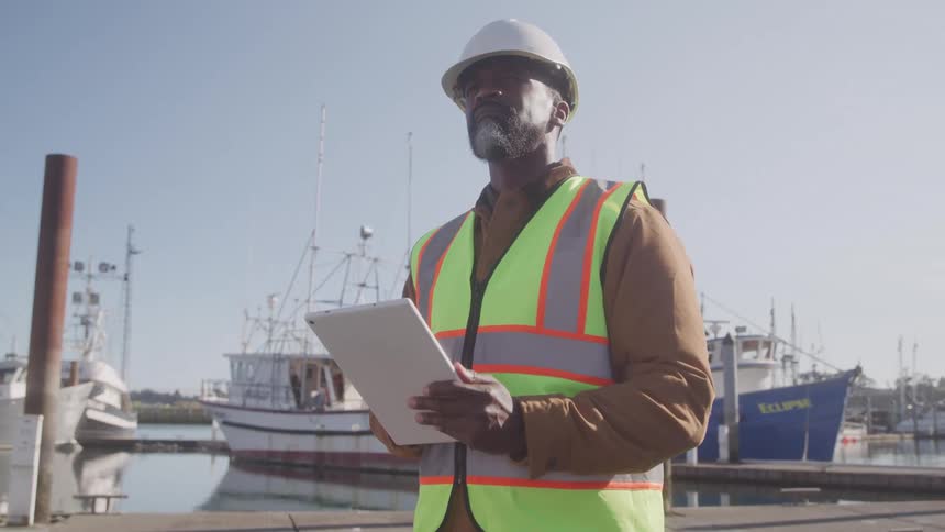 A man standing on a dock near ships using a tablet