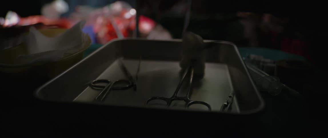 A tray in an operating room holds metzenbaum scissors as doctors drop two others while holding cotton balls