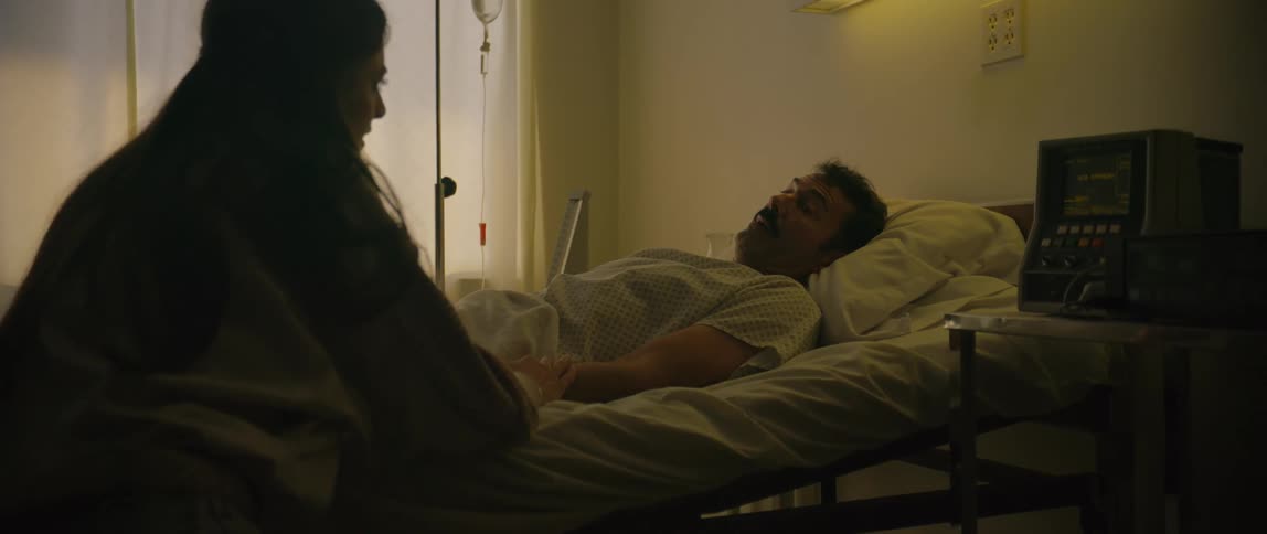 A woman holds a mans hand beside his hospital bed in a quiet caring moment
