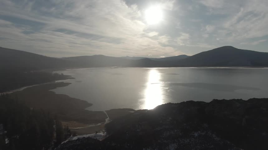 Aerial shot of a lake surrounded by mountains with the sun in the spotlight