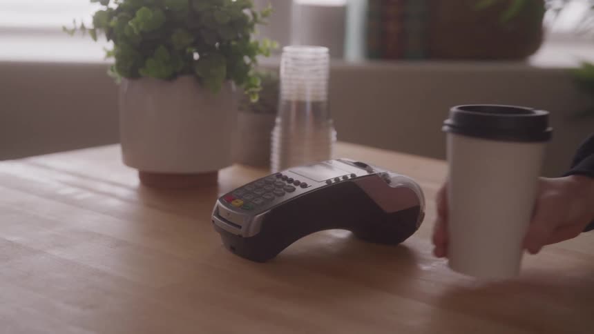 A person pays with a card and receives a coffee cup