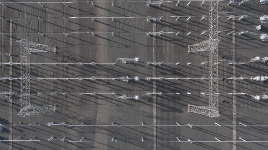 Aerial view of a substation with symmetrical transmission lines and long shadows
