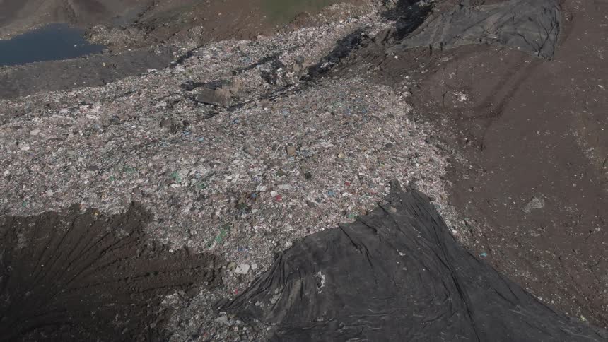 Bulldozers move trash heaped on a hill slope during the daytime