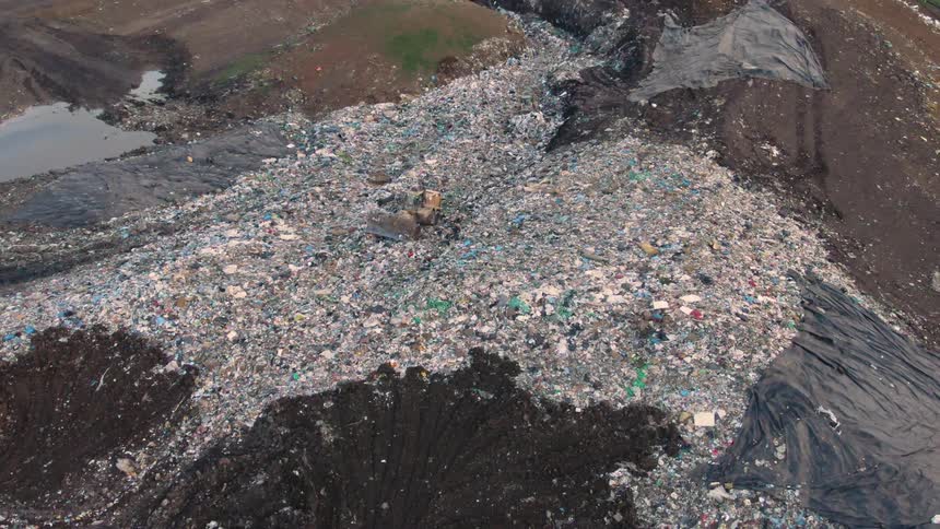 An aerial shot captures a sprawling landfill with heaps of waste and a bulldozer working in the center