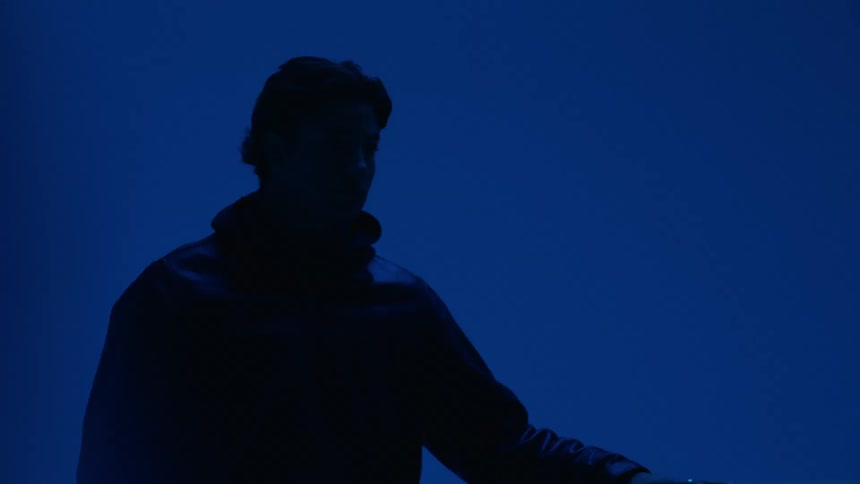 A man stands next to a car inside a garage illuminated by dark blue light