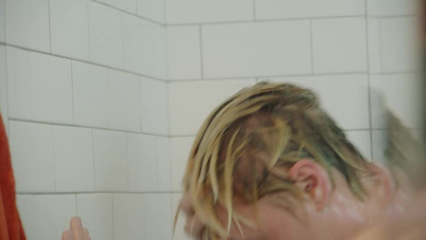 Blonde person dances in a white tiled shower